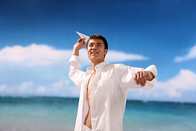 东方男人在海滩扔纸飞机照片
