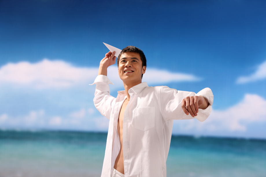 东方男人在海滩扔纸飞机照片 东方男人在海滩扔纸飞机照片