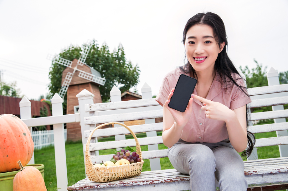 青年女人坐在户外展示手机
