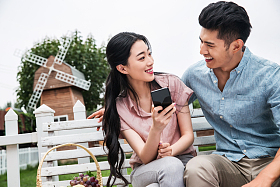 青年伴侣坐在户外看手机照片