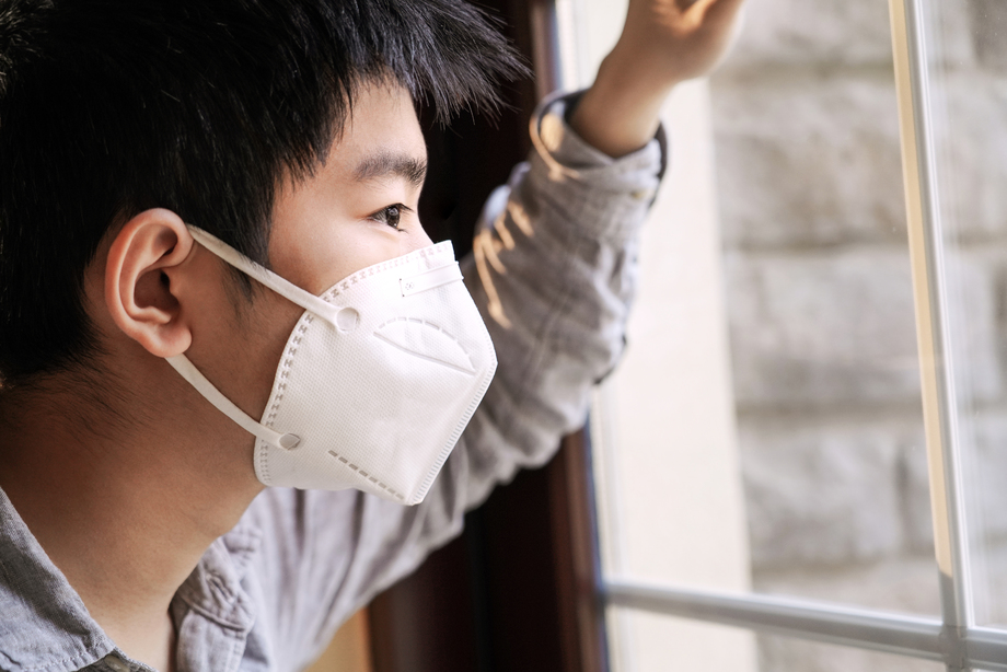 戴口罩的男孩透过窗户往外看