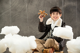 拿着飞机模型坐在行李箱上的男孩