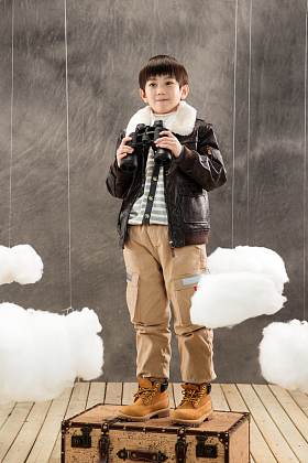 快乐男孩拿着望远镜站在行李箱上