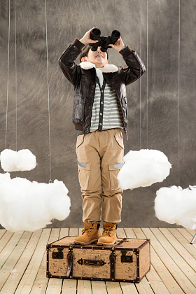 快乐男孩站在行李箱上拿望远镜看远方