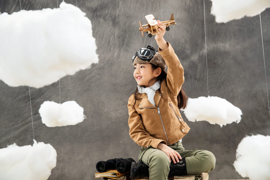 坐在行李箱上快乐的女孩拿着飞机模型 坐在行李箱上快乐的女孩拿着飞机模型