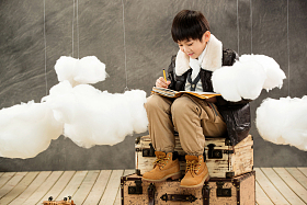 快乐男孩坐在行李箱上写日记图片