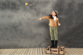 站在行李箱上扔纸飞机的小女孩