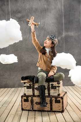 坐在行李箱上的快乐女孩举着飞机模型