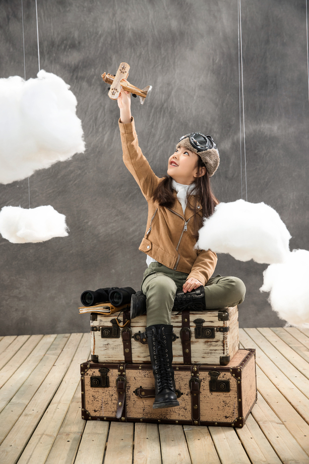 坐在行李箱上的快乐女孩举着飞机模型 坐在行李箱上的快乐女孩举着飞机模型