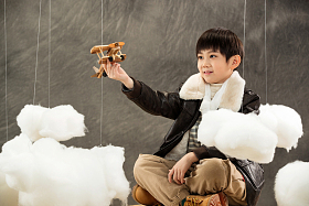 拿着飞机模型坐在行李箱上的男孩