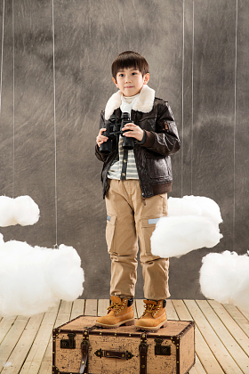 快乐男孩拿着望远镜站在行李箱上