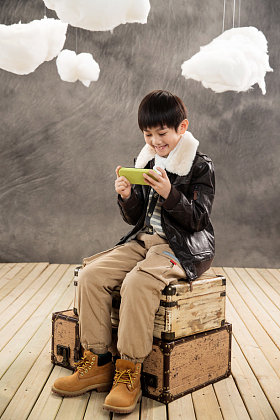 小男孩坐在复古行李箱上玩游戏机