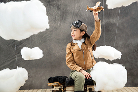 坐在行李箱上的女孩举着飞机模型