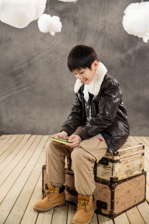 小男孩坐在复古行李箱上玩游戏机
