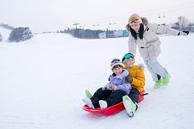 滑雪场上妈妈推着坐在雪上滑板的孩子们