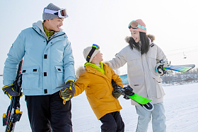 雪场上拿着滑雪板行走的一家三口