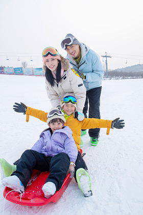 滑雪场上父母推着坐在雪上滑板的孩子们
