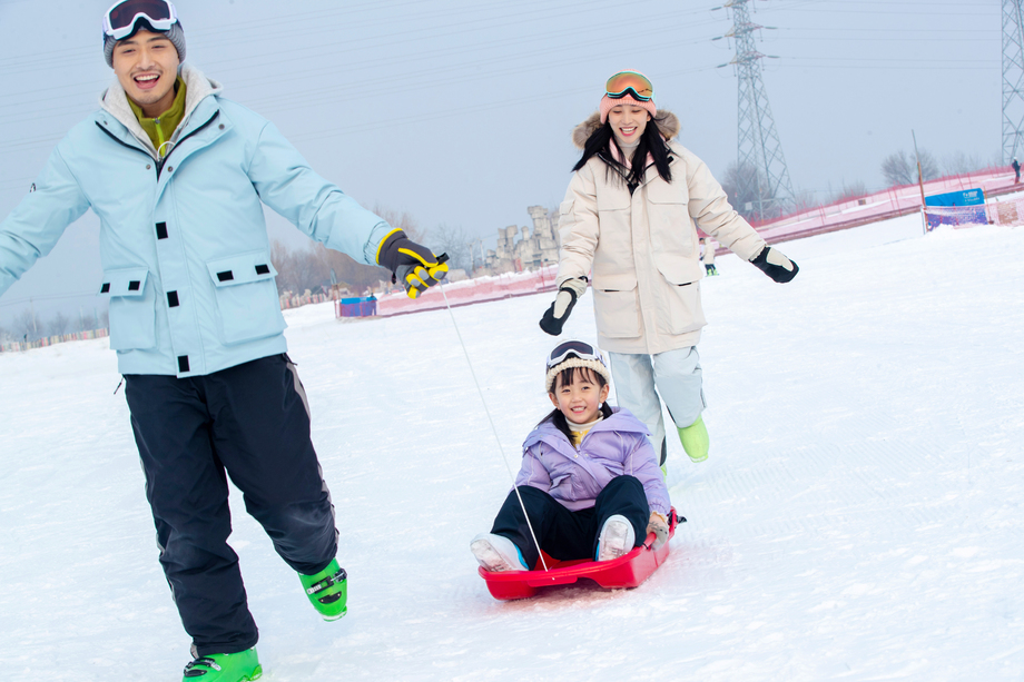 滑雪场上父母和坐在雪上滑板的女儿玩耍 滑雪场上父母和坐在雪上滑板的女儿玩耍
