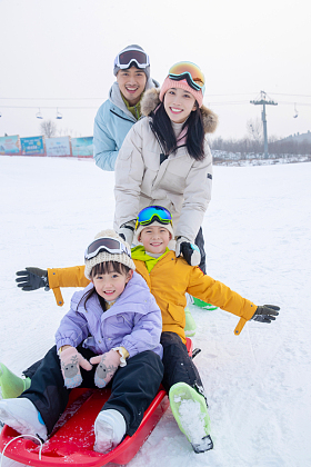 滑雪场上父母推着坐在雪上滑板的孩子们
