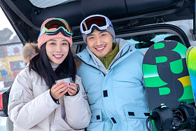 青年伴侣坐在汽车后备箱上喝水