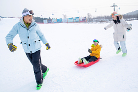 滑雪场上父母和坐在雪上滑板的儿子玩耍