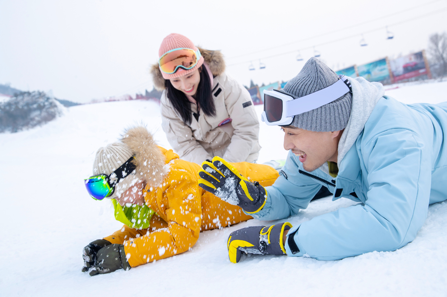 快乐的一家三口趴在雪地上玩雪