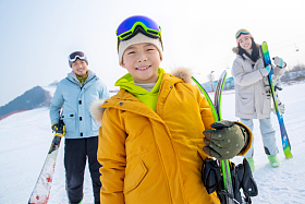雪场上拿着滑雪板的一家三口