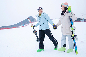 青年伴侣手牵手拿着滑雪板边走边聊