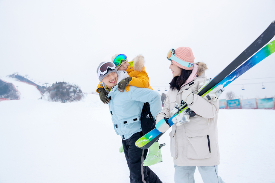 滑雪场上背着儿子的父亲和抱着滑雪板的母亲
