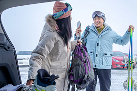 停车场内青年伴侣拿着雪具交谈