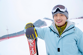 扶着滑雪板的青年男人站在滑雪场上