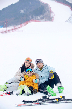 雪场上坐在雪道上的一家三口