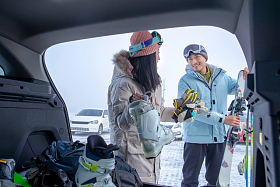 停车场内青年伴侣从汽车后备箱拿滑雪装备