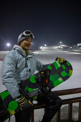 夜晚青年男人抱着滑雪板坐在滑雪场内的护栏上