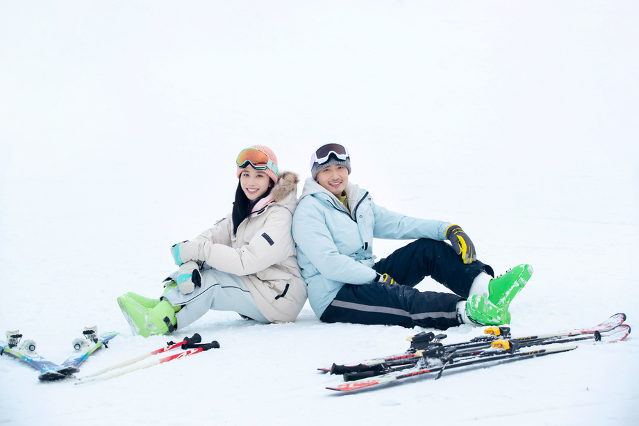 快乐的青年伴侣背靠背坐在雪地上