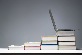 桌子上摆放着从低到高的教科书和笔记本电脑