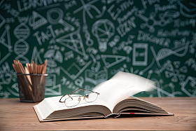 黑板画前的桌子上打开的书和笔筒眼镜