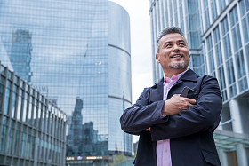 拿着手机的中老年商务男士站着楼群中间