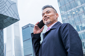 中老年商务男士站着楼群中间打电话