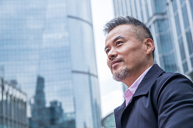 中老年商务男士站着楼群中间照片