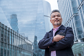 拿着手机的中老年商务男士站着楼群中间