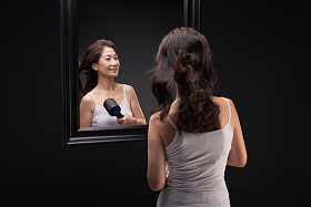 中年女人对着镜子用吹风机吹头发