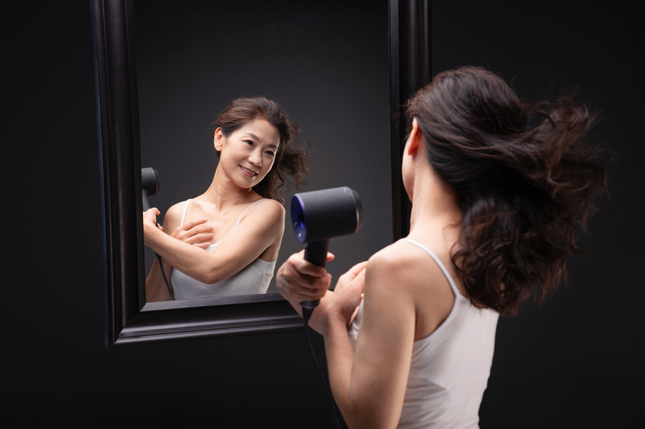 中年女人对着镜子用吹风机吹头发 中年女人对着镜子用吹风机吹头发