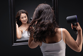 中年女人对着镜子用吹风机吹头发