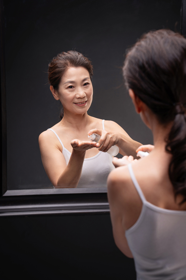 优雅的中年女人对着镜子喷爽肤水