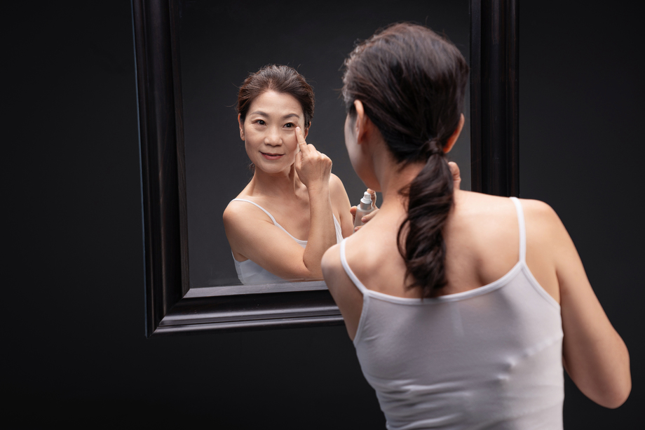 优雅的中年女人对着镜子涂抹爽肤水 优雅的中年女人对着镜子涂抹爽肤水