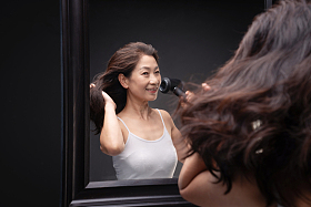 中年女人对着镜子用吹风机吹头发