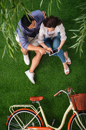 青年伴侣坐在草地上使用平板电脑