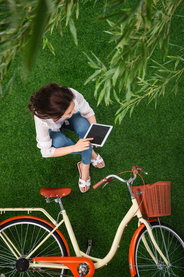 坐在草地上使用平板电脑的青年女人 坐在草地上使用平板电脑的青年女人