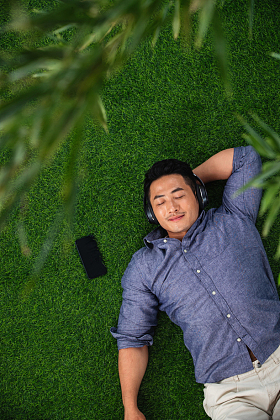 躺在草地上听音乐的青年男人